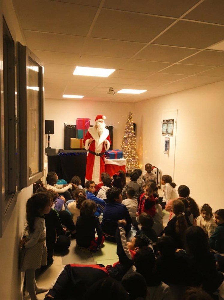 Des dizaines d'enfants assis au sol, le Père Noël au fond de la salle.