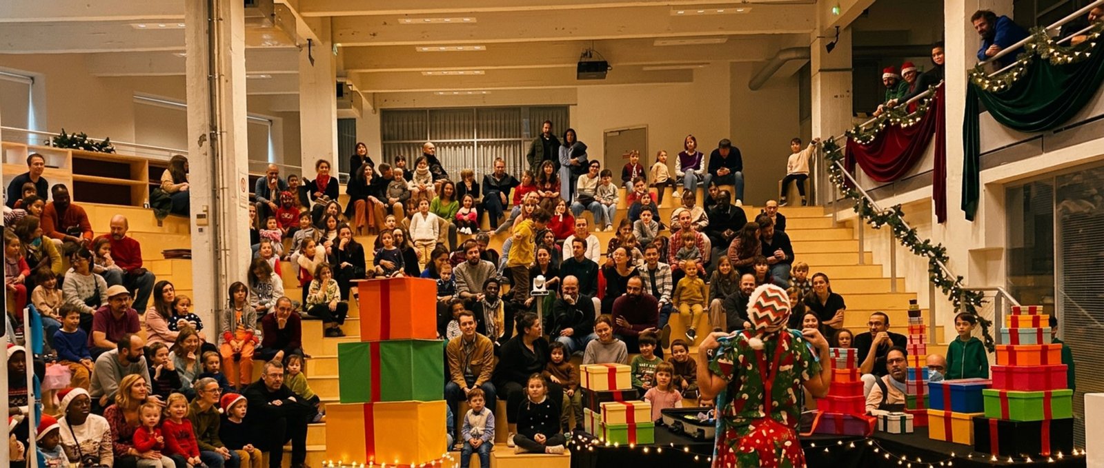 Gradins pleins d'enfants et de familles, la pyramide de cadeaux au centre de la scène.